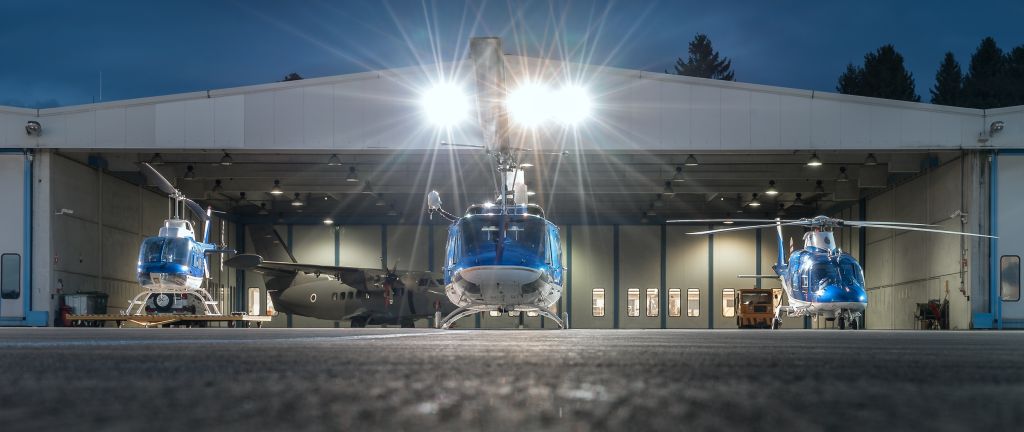 Trije policijski helikopterji zvečer na ploščadi pred hangarjem Letalske policijske enote