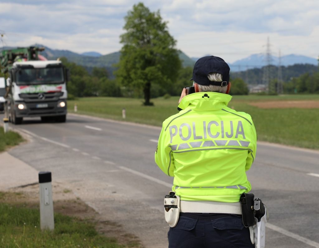 Prometna policistka stoji ob cesti in meri hitrost z ročnim radarjem.