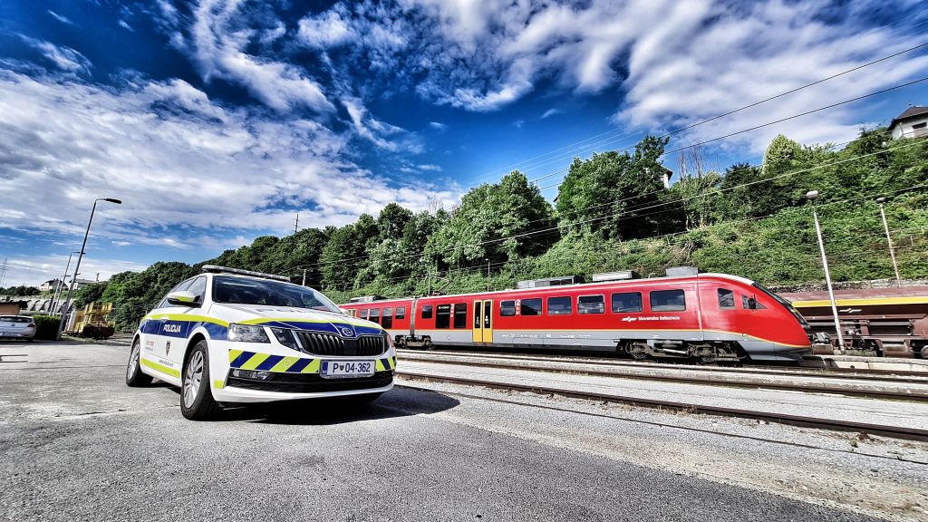 slika policijskega vozila vzporedno z železniško progo z vlakom