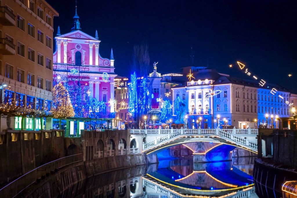 Praznično okrašeno središče Ljubljane, pogled z reke na modro osvetljeno Tromostovje ponoči