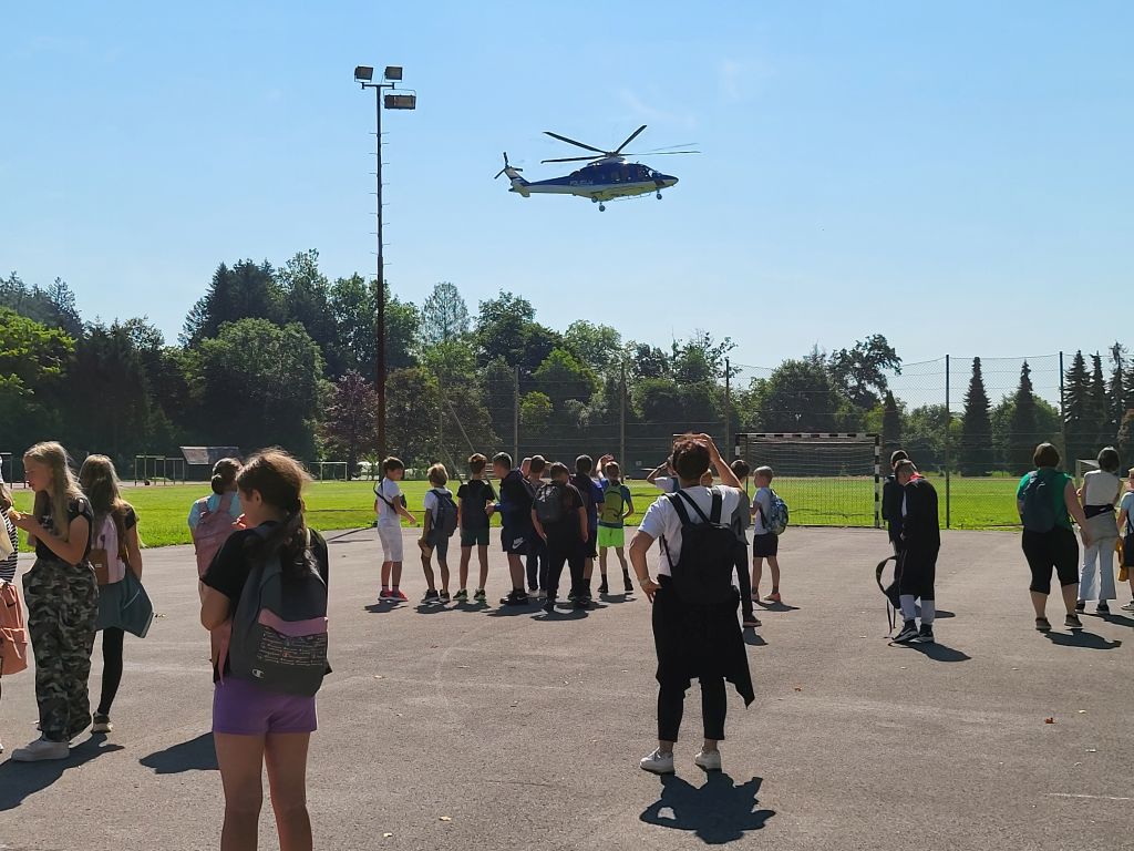 Otroci si na policijskem poligonu ogledujejo prelet helikopterja.