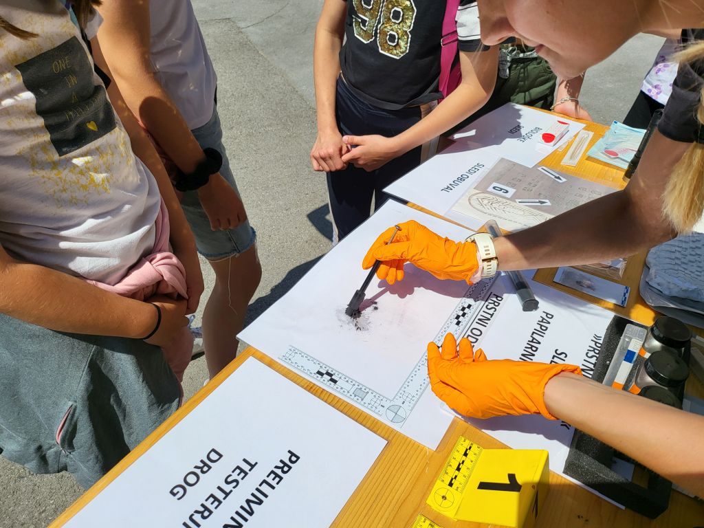 Kriminalistka otrokom kaže, kako se jemljejo prstni odtisi.
