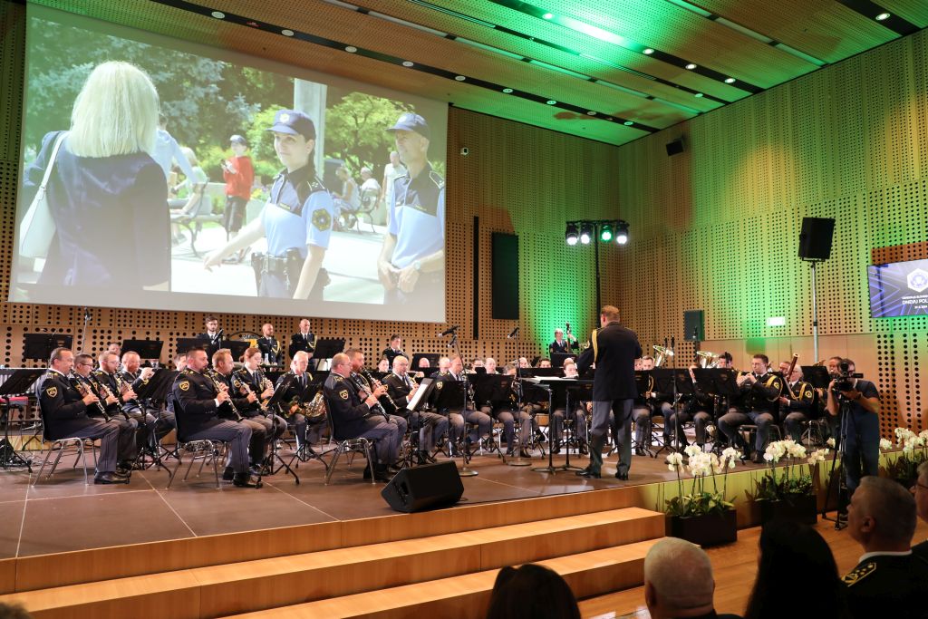 Videoprikaz policijskega dela med igranjem Policijskega orkestra na odru