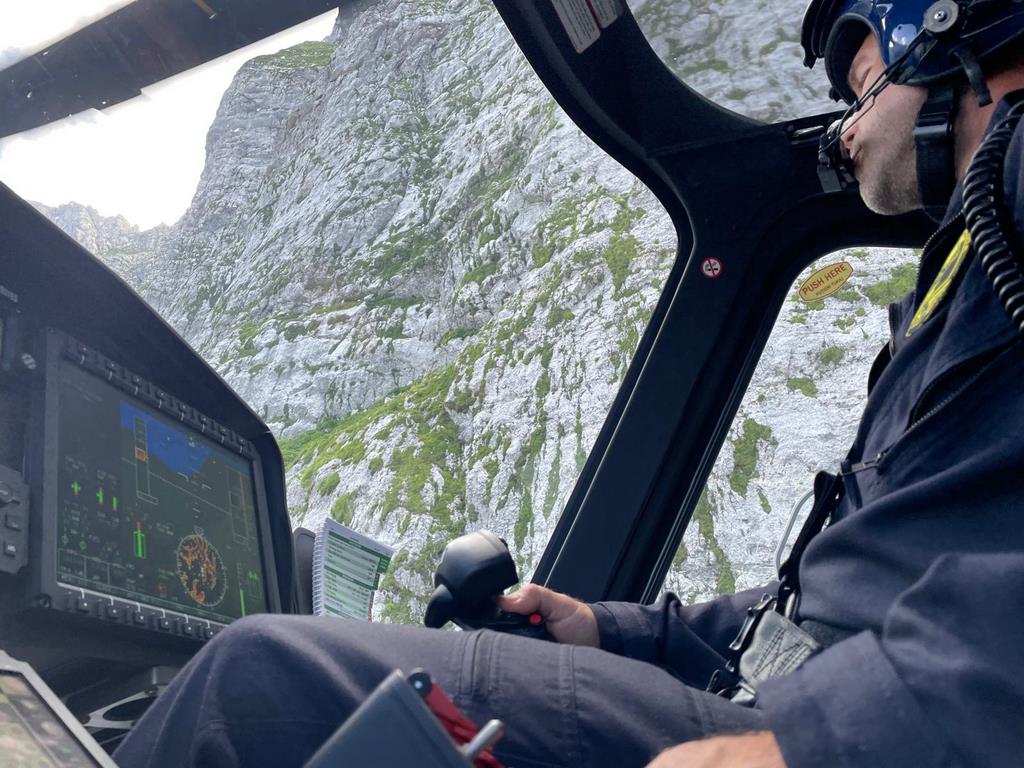 Pilot helikopterja med letenjem, pogled iz kabine na skalne stene ob njem