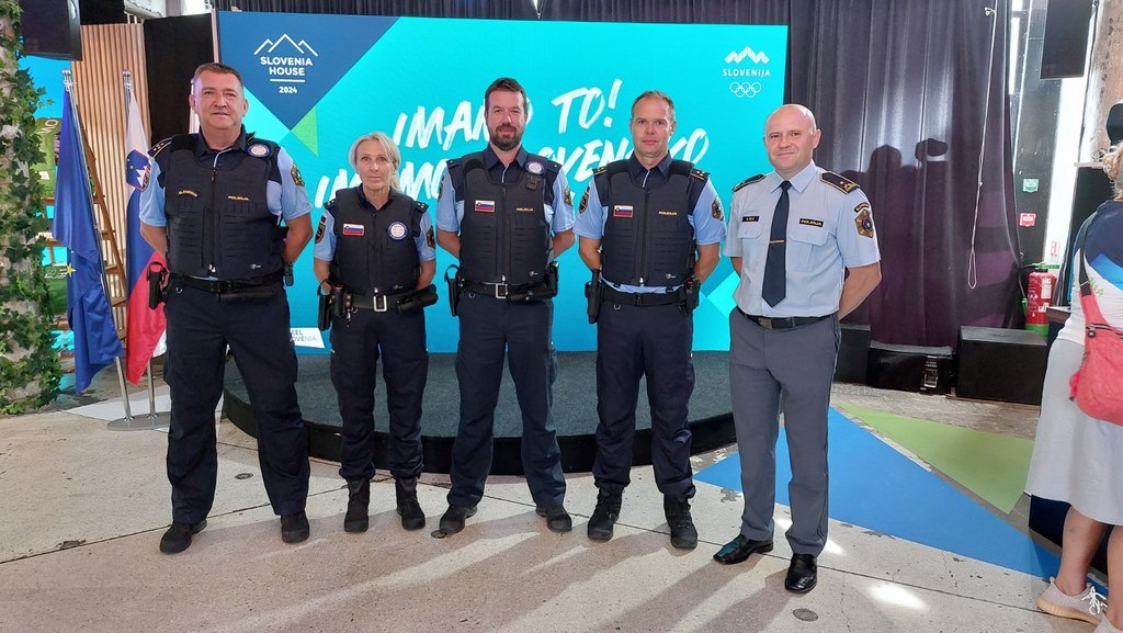 Skupinska slika petih slovenskih policistov, stojijo pred plakatom Slovenske hiše v Parizu