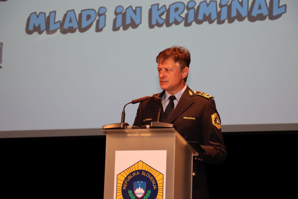 Namestnik generalnega direktorja policije mag. Robert Ferenc med nagovorom, v ozadju projekcija z naslovom posveta