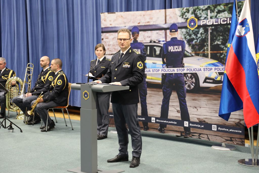 Damjan Petrič med nagovorom, za njim so promocijski pano policije, zastave in kvintet Policijskega oprkestra