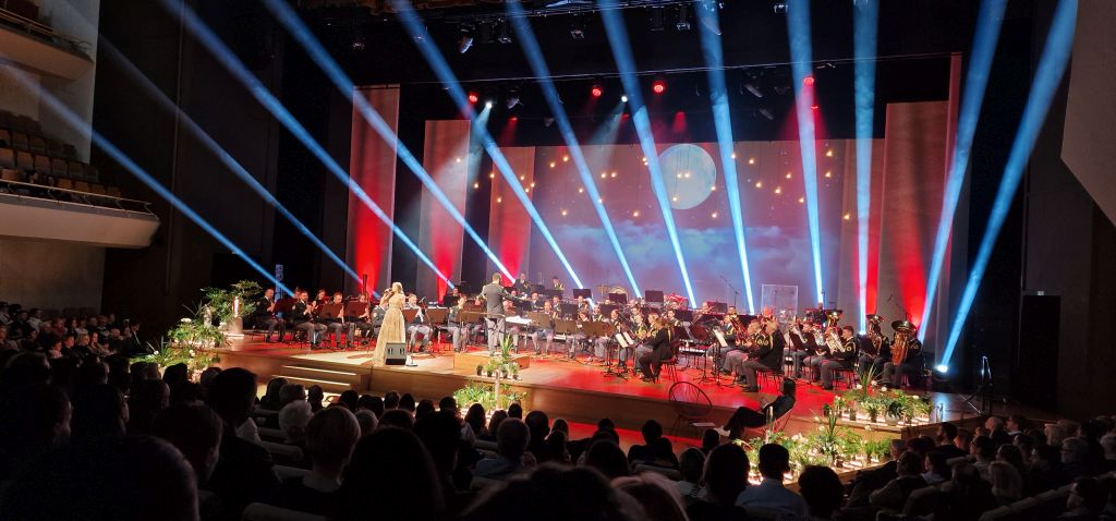 Med koncertom, na sliki je celoten orkester na odru s slistko Lešnjek, v ospredju občinstvi v parterju