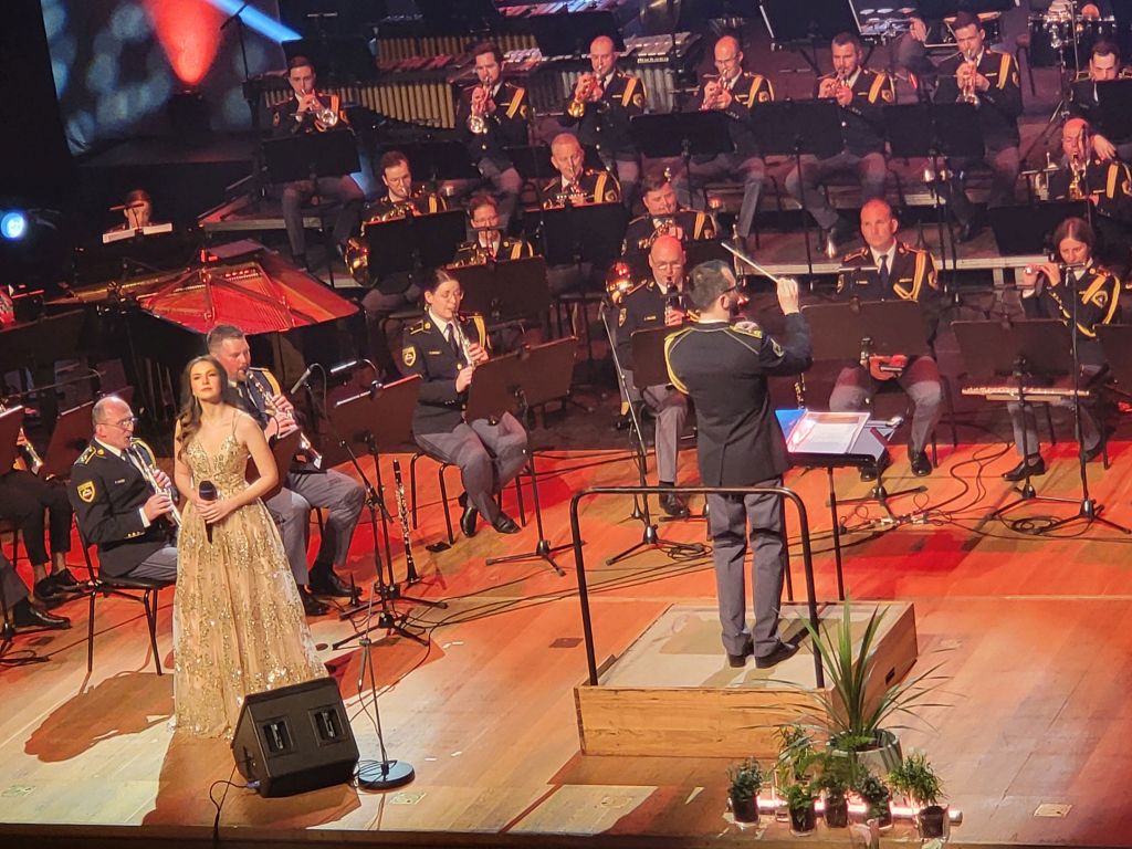 Saša Lešnjek med petjem, ob njej člani orkestra in dirigent