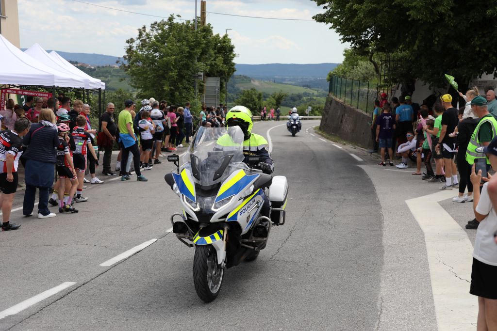 Policist motorist se pelje po kolesarski trasi, ob strani stojijo navijači.