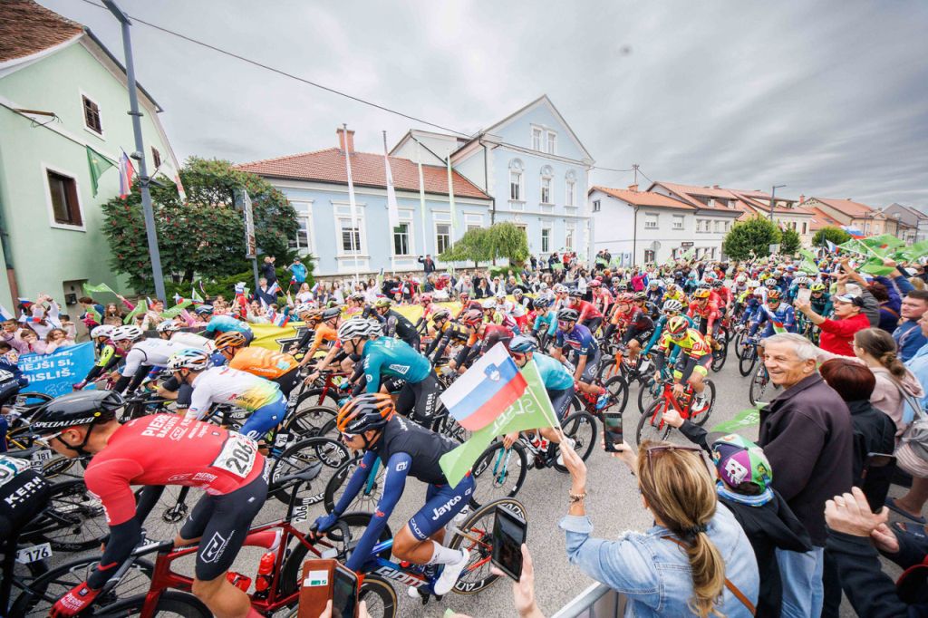 Množica kolesarjev vozi čez mesto, ob progi množica navijačev z zastavami.Foto: spletna stran Tour of Slovenia