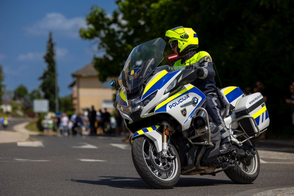 Policist motorist med vožnjo po progi kolesarske dirke, v ozadju gledalci stojijo ob progi.