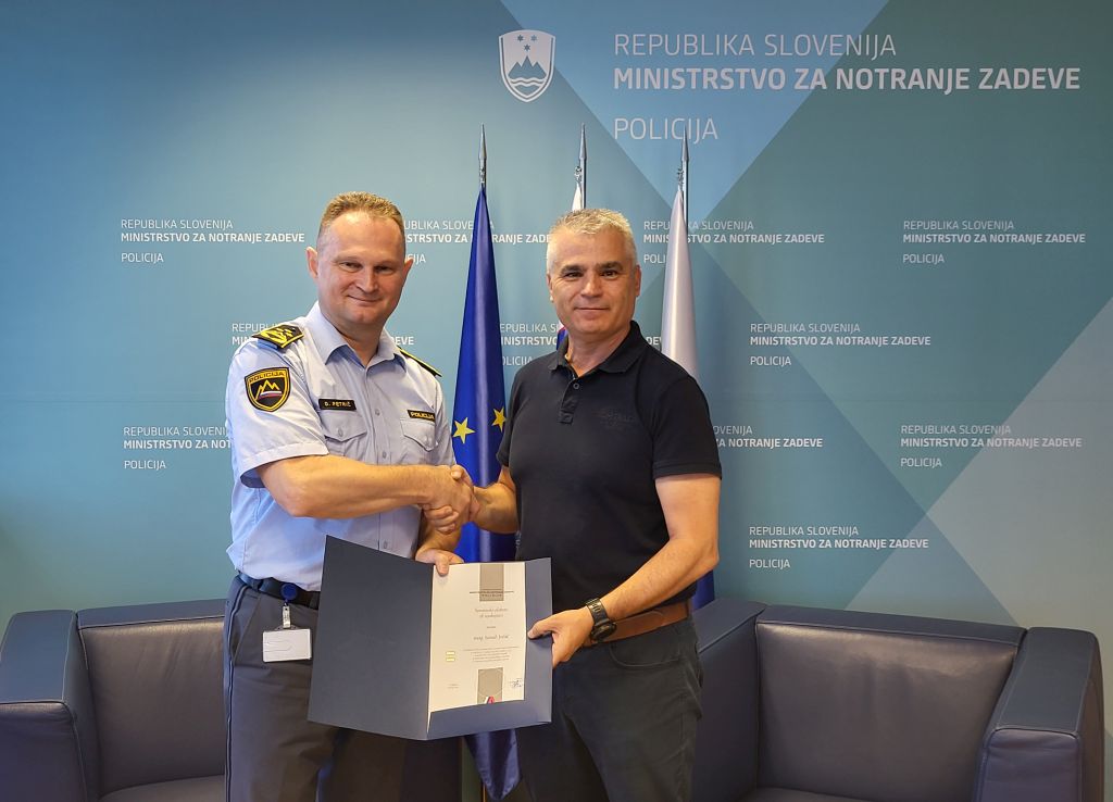 Petrič in Jušić se rokujeta, za njima so zastave.