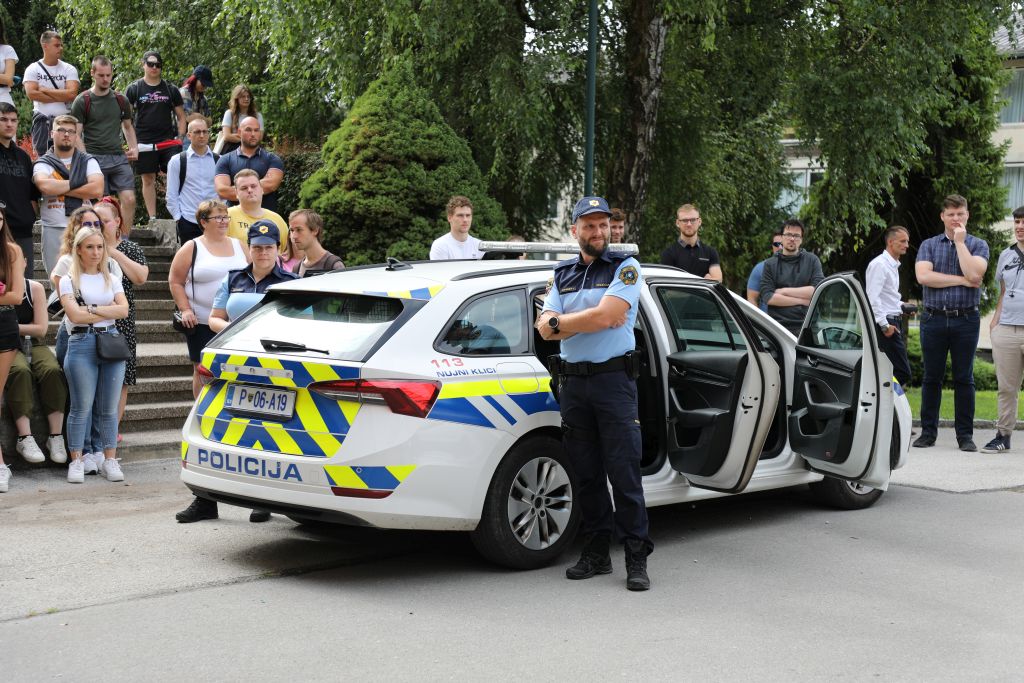Policist stoji ob policijske avtu, okoli njega je množica obiskovalcev.