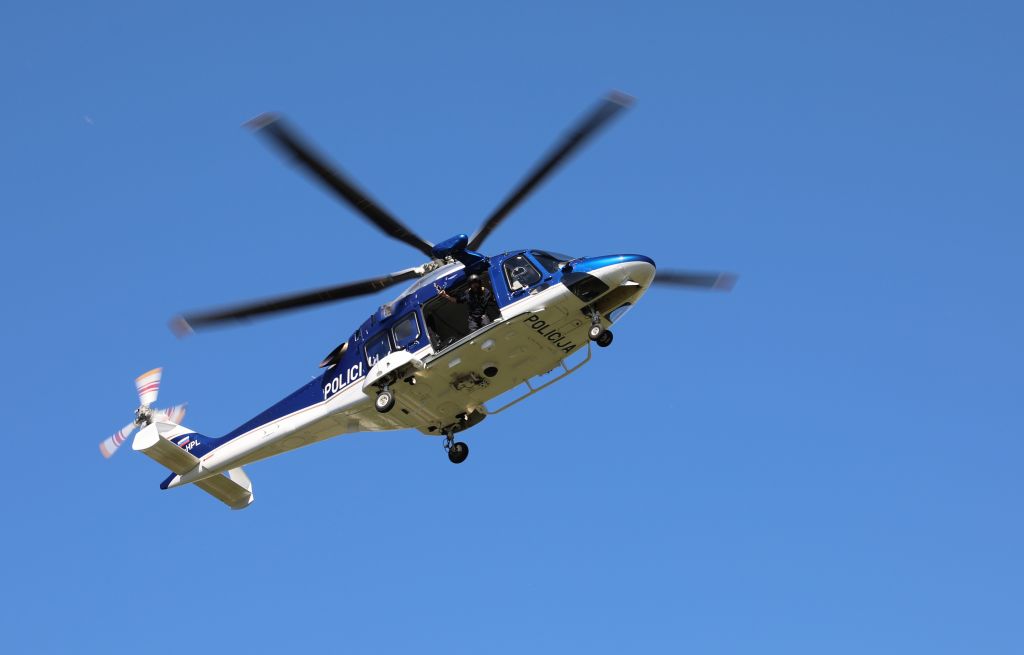 Policijski helikopter v zraku; v ozadju je jasno modro nebo.