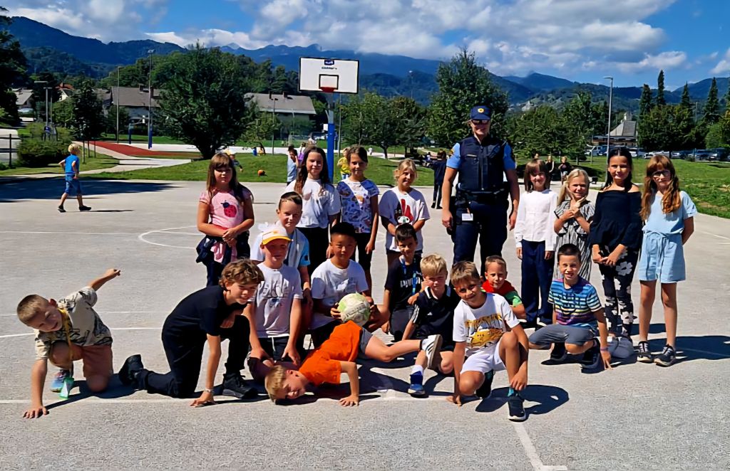 Policistka skupaj s skupino otrok na igrišču pred šolo nja Bledu