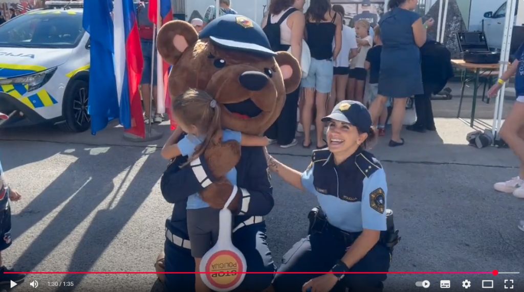 A girl hugs Pika, the police mascot, and next to her is smiling policewoman (video excerpt)