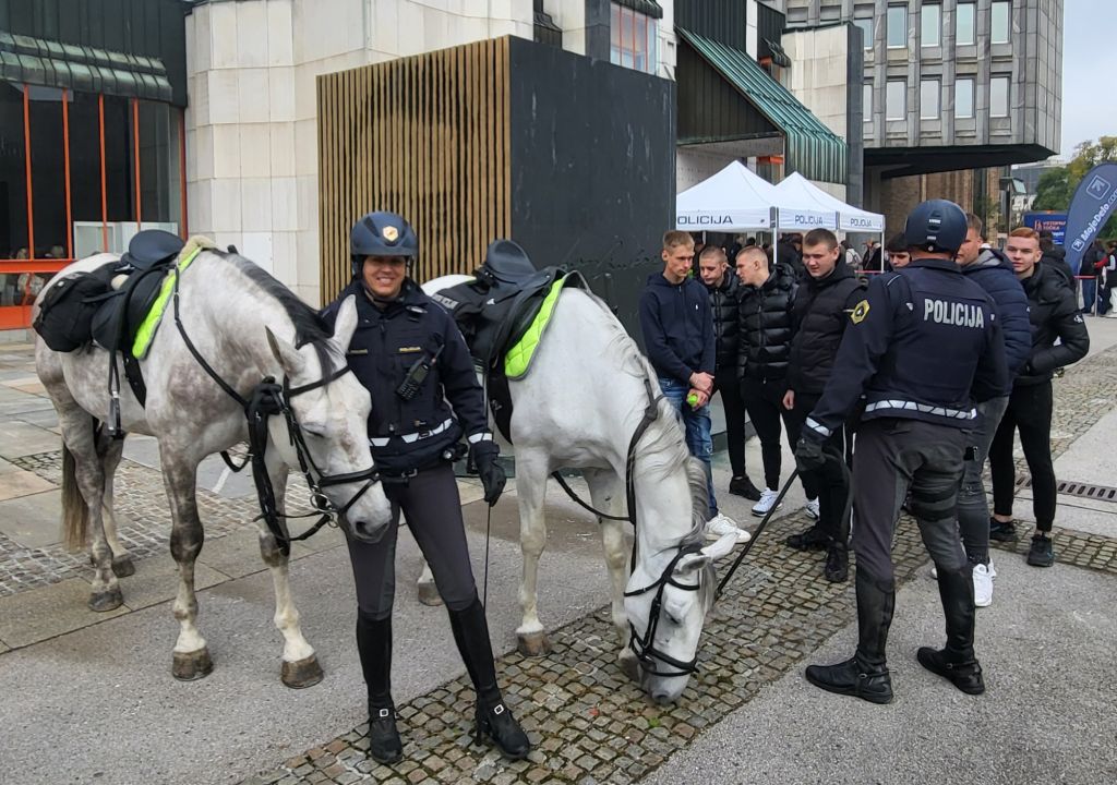 Policista ob policijskih konjih se pogovarjata s skupino mladih