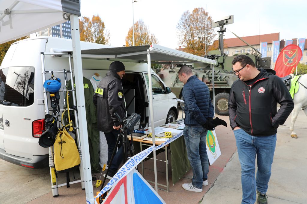 Obiskovalca si ogledujeta policijsko vozilo in razstavljeno opremo na ploščadi.