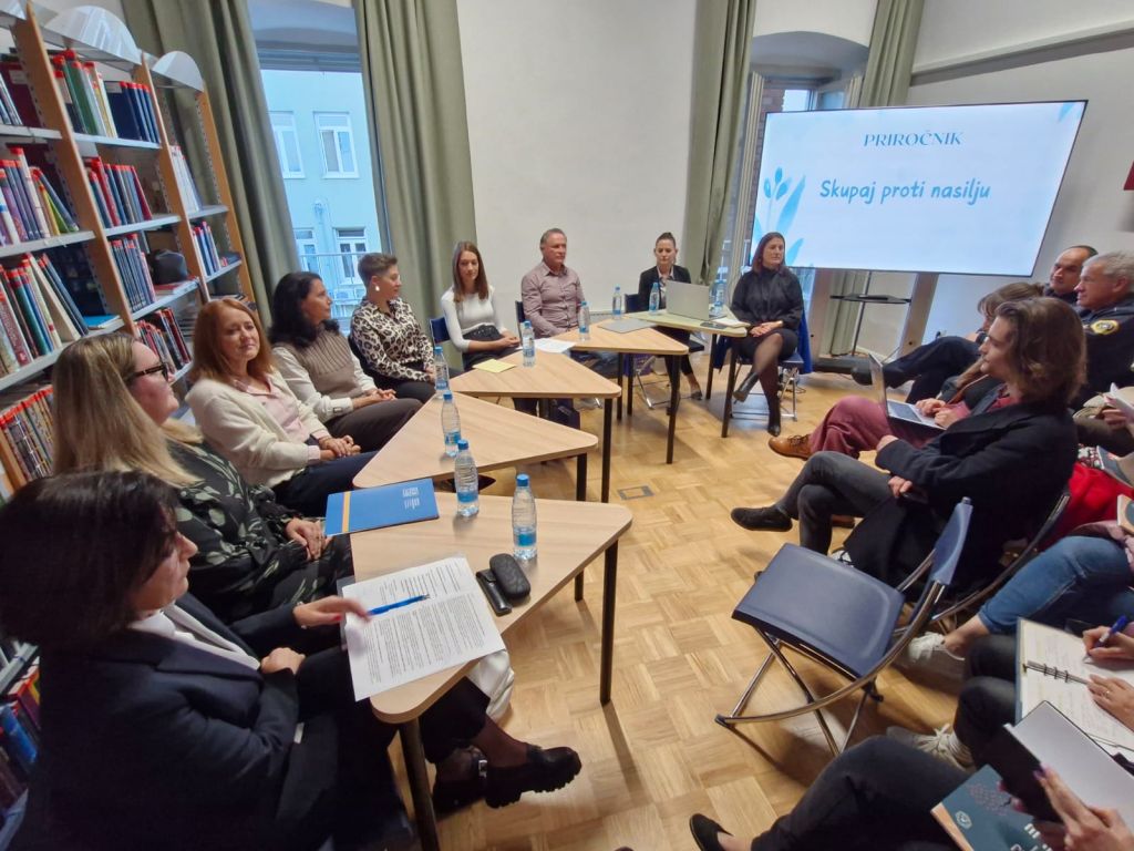 Polna dvorana sodelujočih okoli omizja in poslušalcev