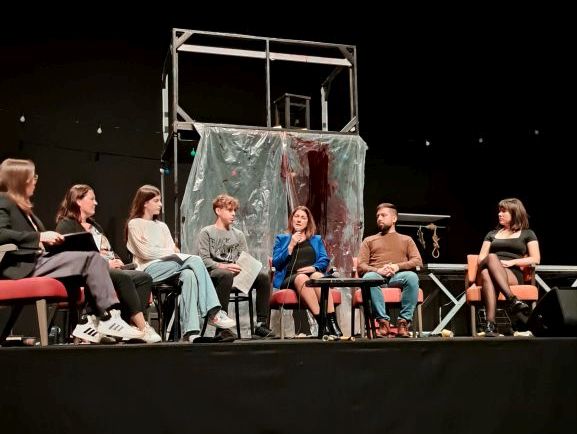 Sodelujoči na okrogli mizi, sedijo na odru, obrnjeni so proti publiki