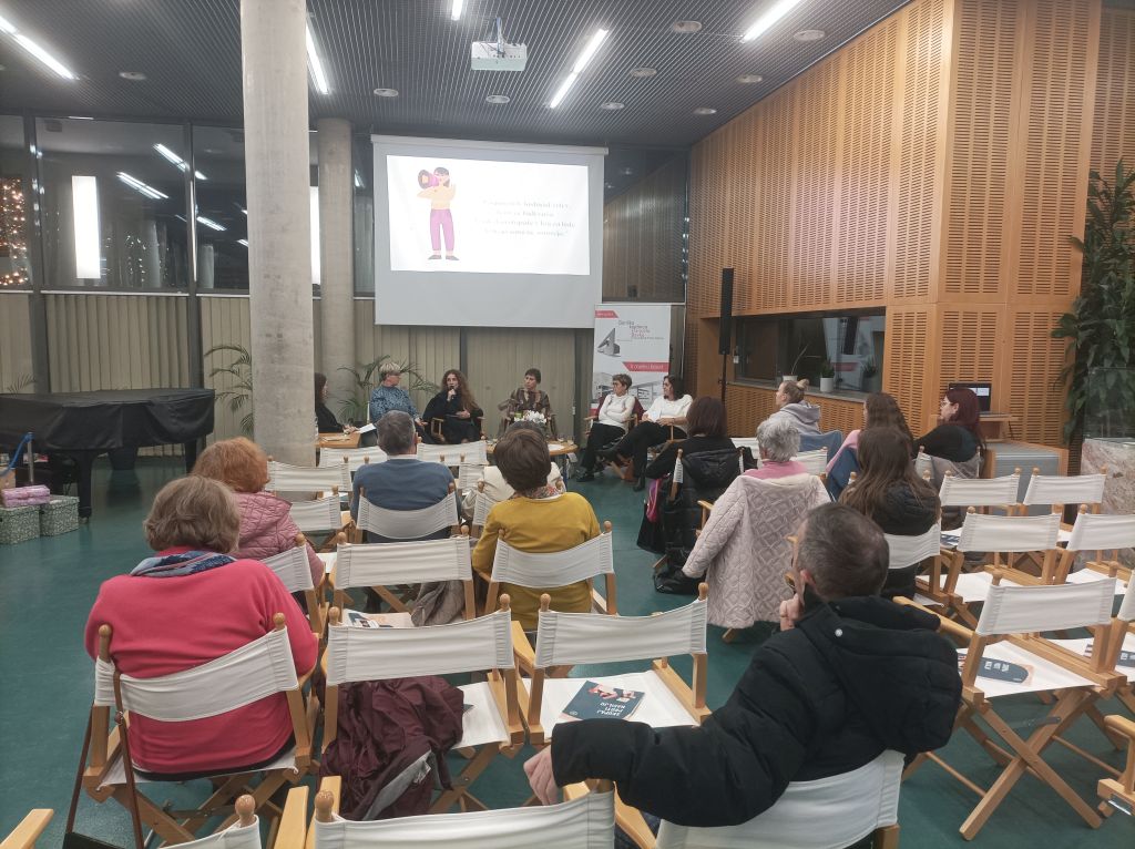 Poslušalci sedijo v dvorani, na odru je omizje petih govork.