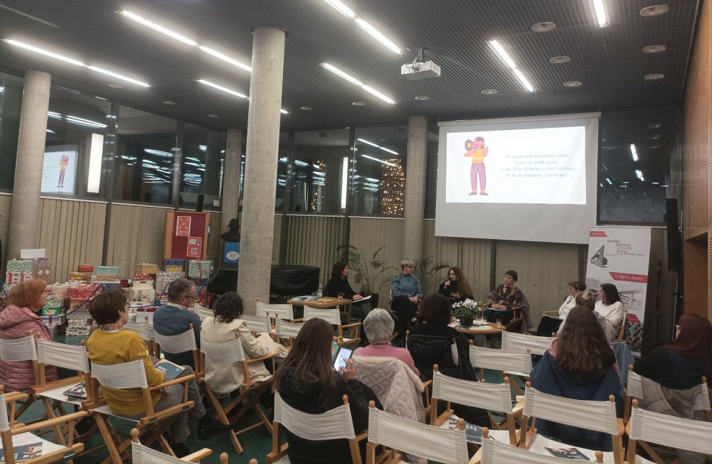 Poslušalci sedijo v dvorani, na odru je omizje petih govork.