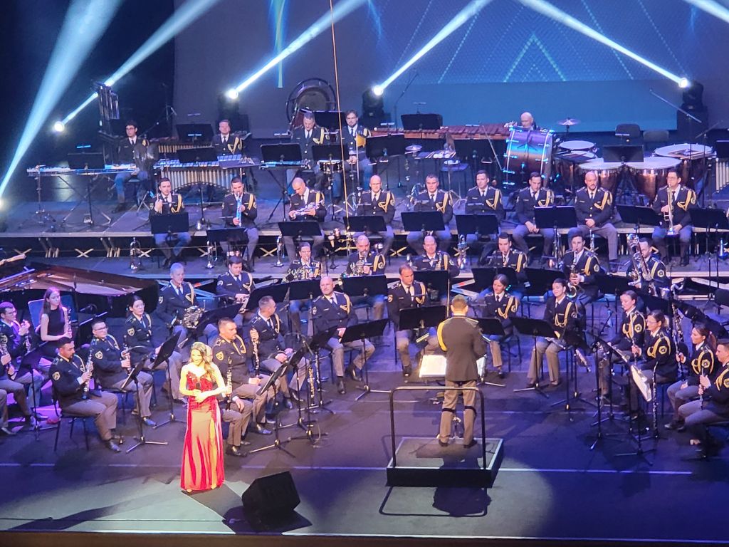 Policijski orkester igra, v ospredju stoji pevka Monika Avsenik v rdeči obleki