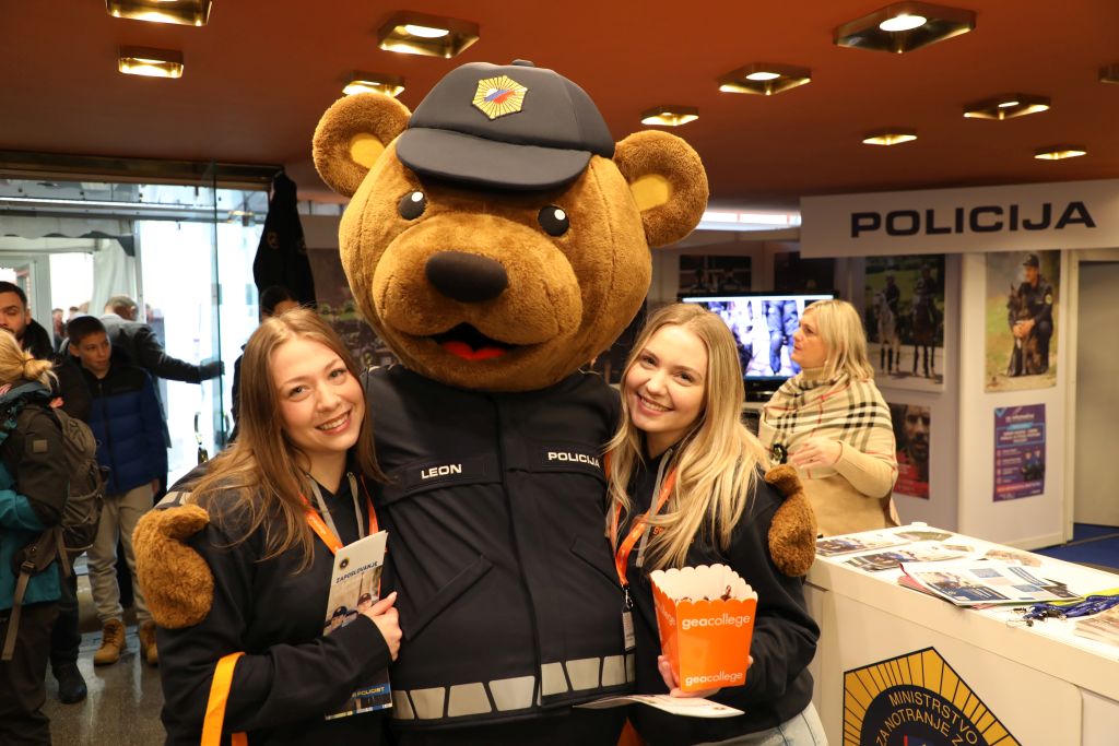 Nasmejani mladi obiskovalki pozirata ob policijski maskoti, medvedu Leonu
