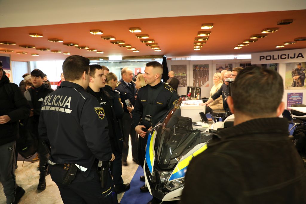 Policist se na razstavnem prostoru policije pogovarja z obiskovalci.