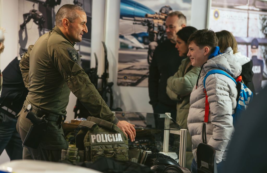 Policist Specialne enote v pogovoru z nasmejanim fantom, okrog njiju gneča obiskovalcev