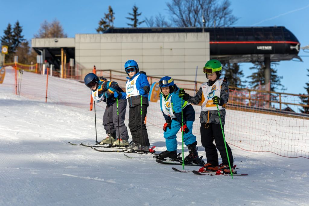 Štirje otroci na smučeh stojijo na zasneženem pobočju