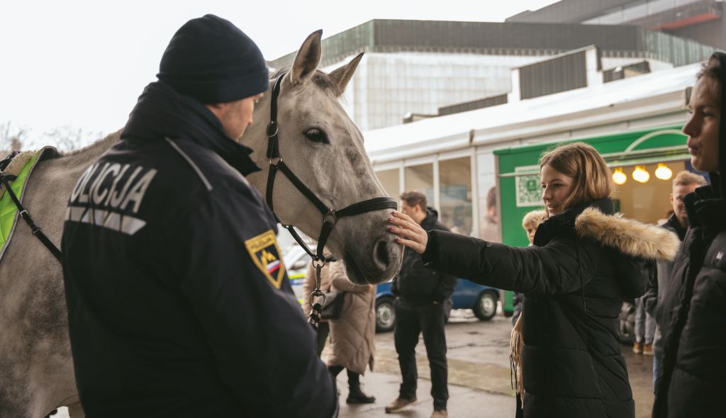 Obiskovalka boža policijskega konja po glavi, ob konju stoji policist.