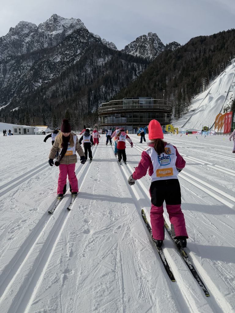 Otroci tečejo na smučeh po snegu.