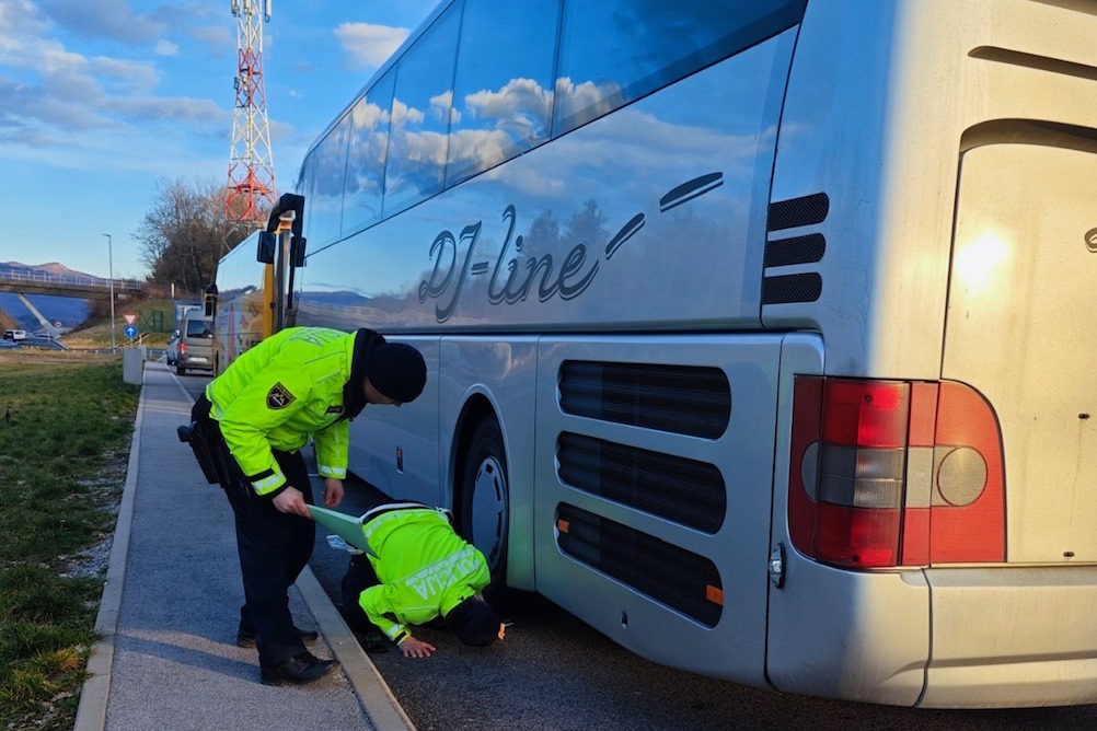 Two police officers are inspecting the undercarriage of a bus