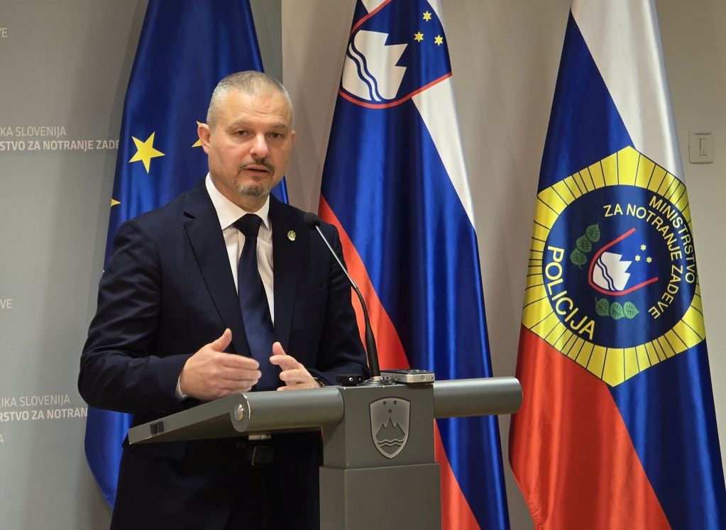 Darko Muženič med izjavo za javnost - stoji za govornico, v ozadju so zastave.