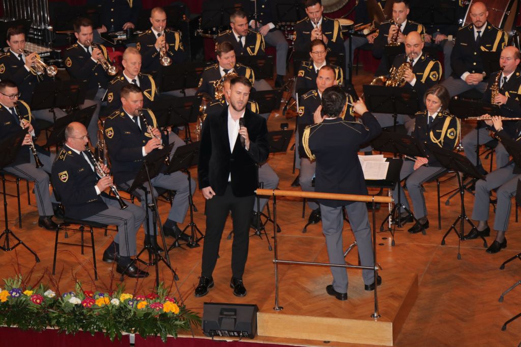 Pevec Gregor Ravnik med petjem, ob njem dirigent, spremlja ga Policijski orkester