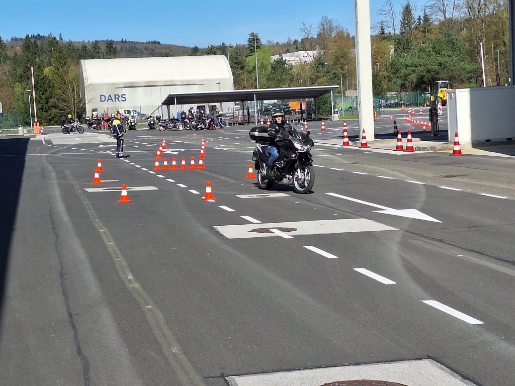 Motorist vozi na Darsovem poligonu, njegovo vožnjo v ozadju spremlja policist