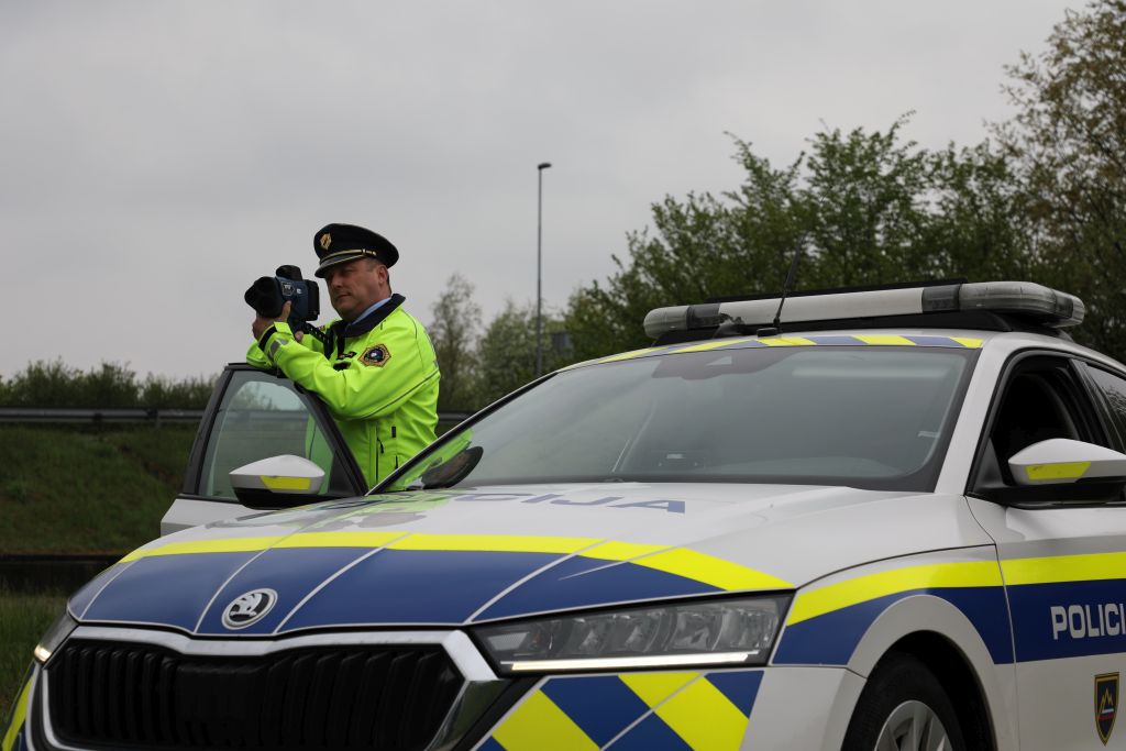 Prometni policist stoji ob patruljnem vozilu in meri hitrost z radarjem.