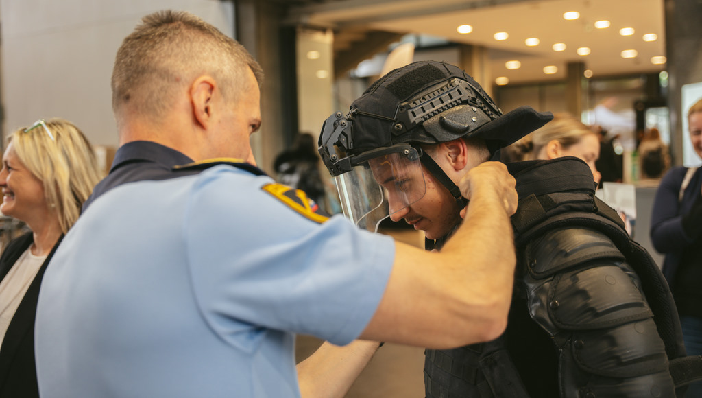 Policist oblači obiskovalca v zaščitno opremo