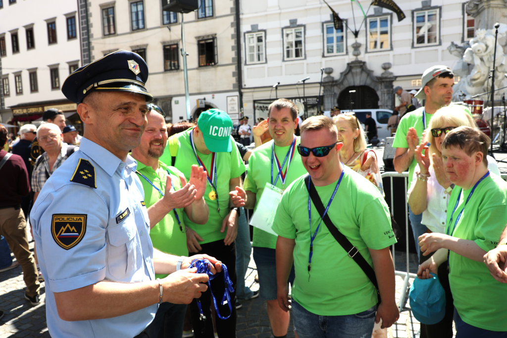 Predstavnik policije v pogovoru s skupino nasmejanih mladih obiskovalcev s posebnimi potrebami