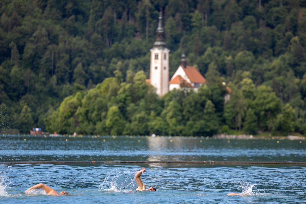 Tekmovalci plavajo v blejskem jezeru, v ozadju otok s cerkvijo