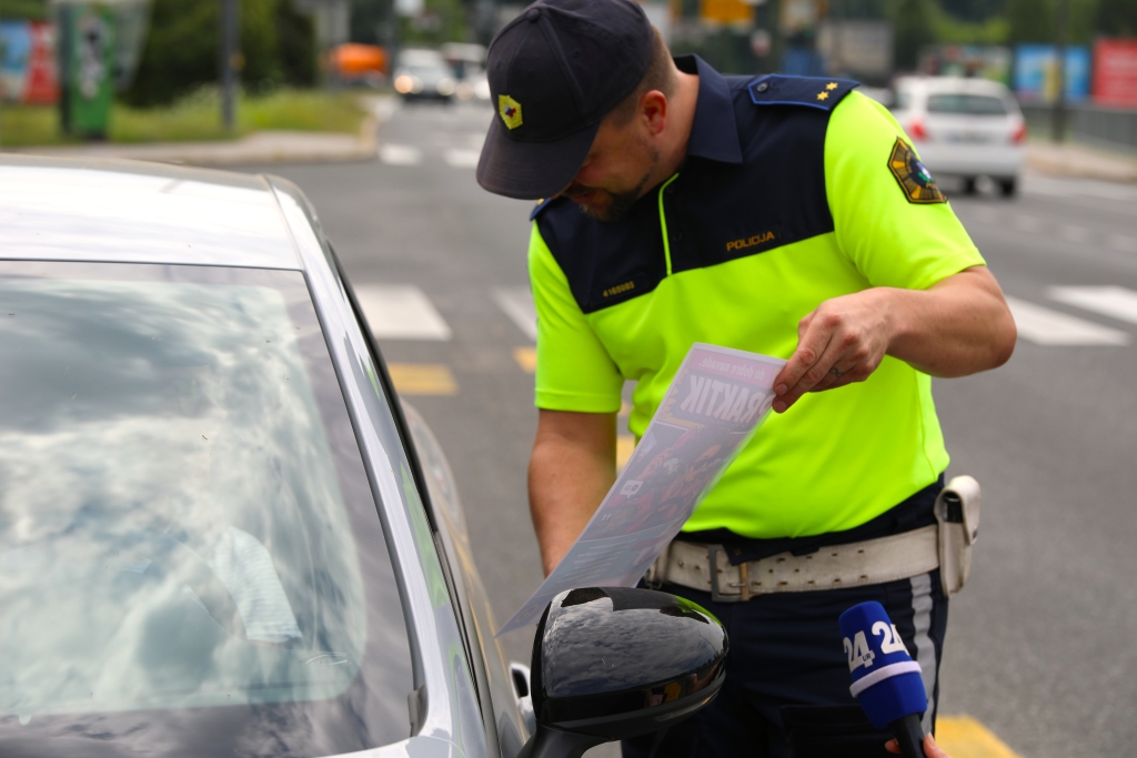 Policist vozniku, ki sedi v avtu, kaže plakat kampanje #častnaprometna