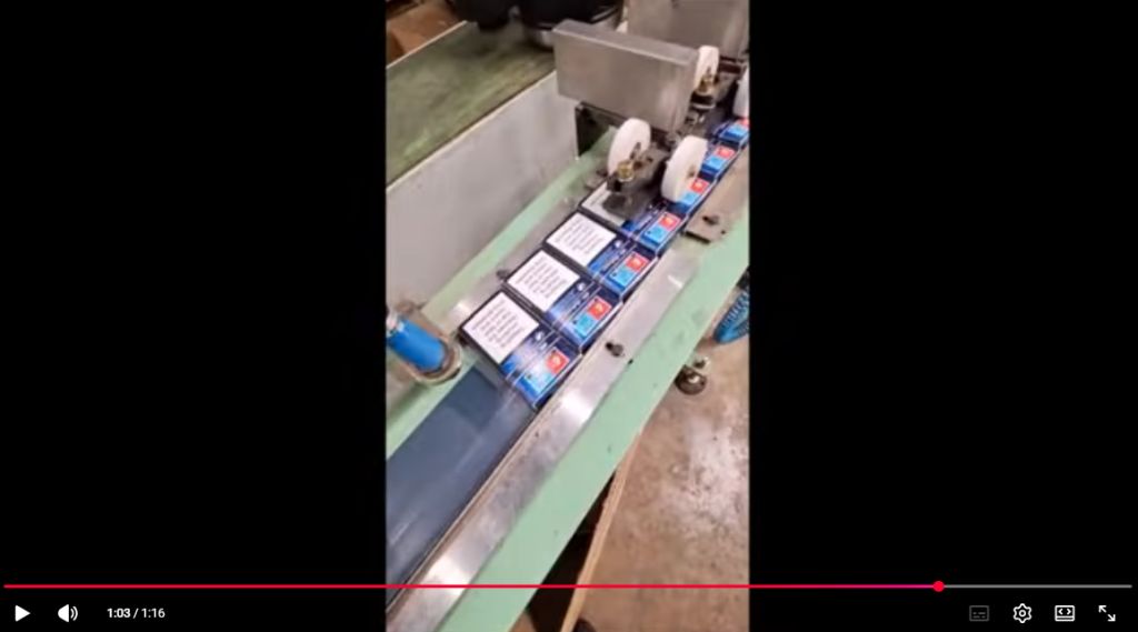 Video, zajem slike prikazuje tekoči trak, na katerem so škatlice cigaret