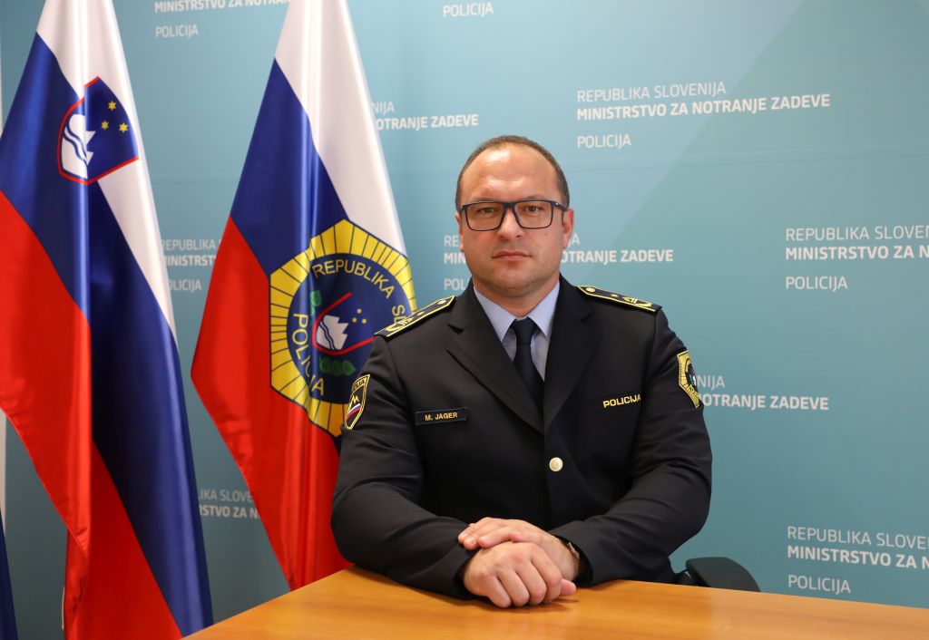 Mitja Jager sedi za mizo, v ozadju zastava Policije in slovenska zastava