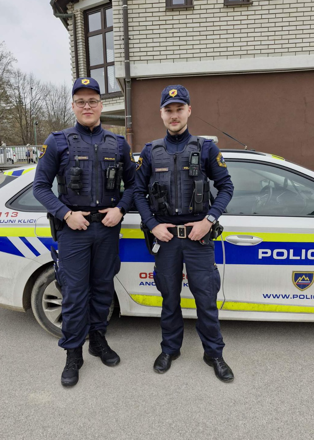 Policista Aljaz Ovčjak in Bine Urleb stojita ob patruljnem vozilu policije.
