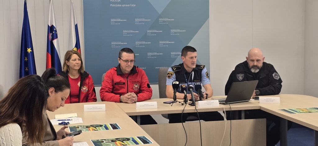 Sodelujoči govorci med novinarsko konferenco, sedijo pred mikrofoni za mizo.