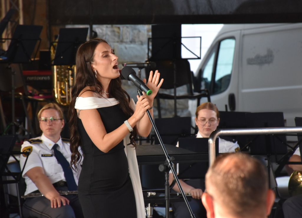 Solistka Mia Guček med petjem na odru, v ozadju na sliki so člani Policijskega orkestra.