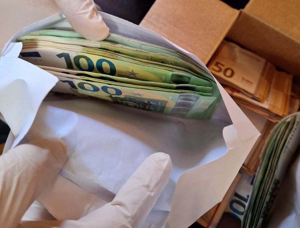 Kriminalist z gumijastimi rokavicami odpira kuverto, v kateri so ponarejeni stoevrski bankovci