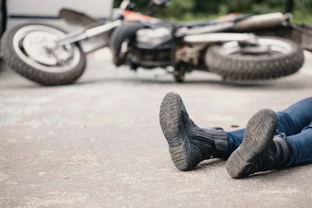 Na sliki so vidne noge motorista, ki leži ob motorju na tleh. Slika je simbolična.